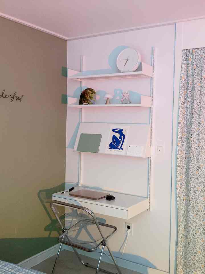 Compact home office space in white and beige tones featuring wall shelves and a transparent chair, creating a minimal and cozy atmosphere