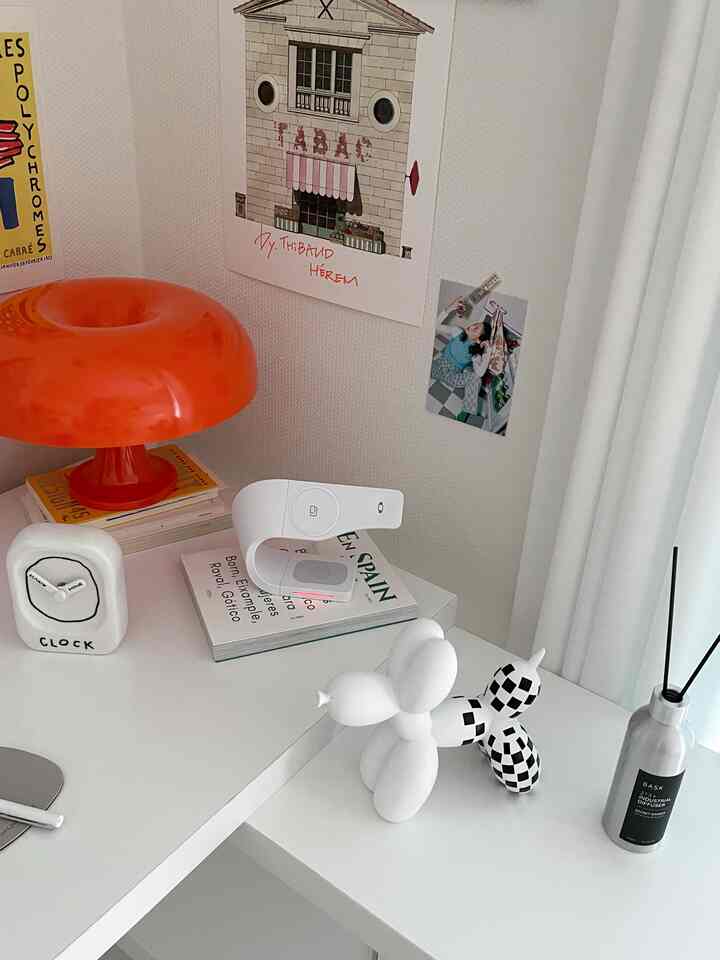 Simple home office space with white and orange tones, featuring a desk, table lamp, objets, clock, and diffuser