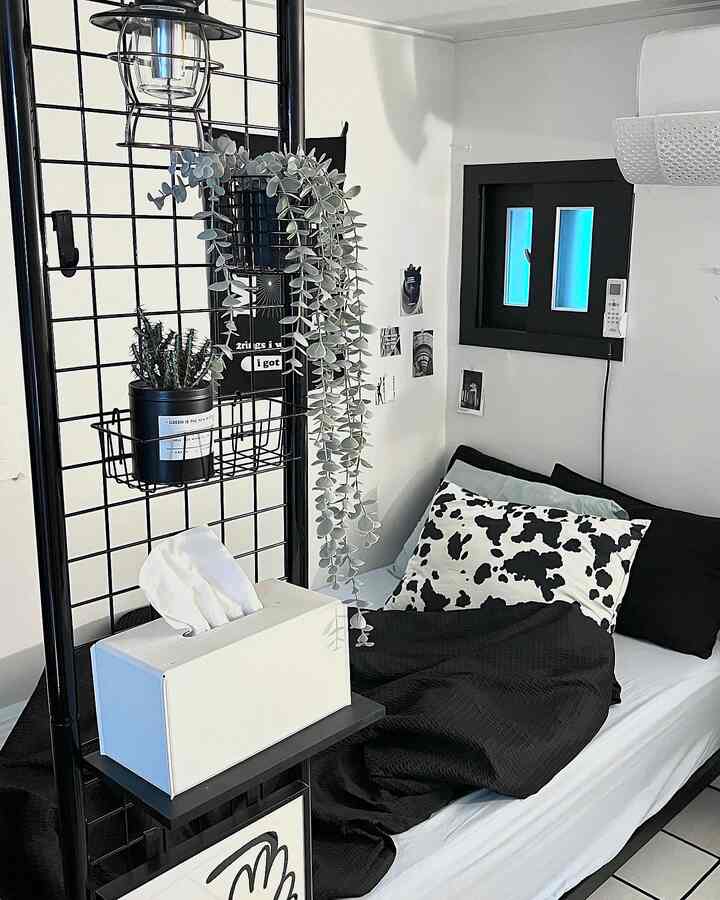 Black and white bedroom featuring a black metal shelf with plants and a bed with monochrome bedding