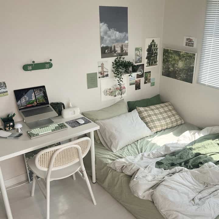 Small single household bedroom with white walls and green bedding, featuring a desk and bed in a natural modern layout