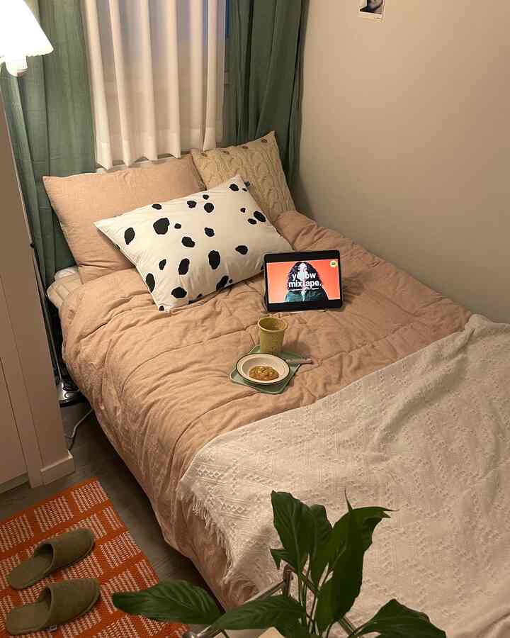 ライトブラウンとグリーンの色調の寝室、快適なベッドやクッション、カーテンと植物が配置された雰囲気ある空間