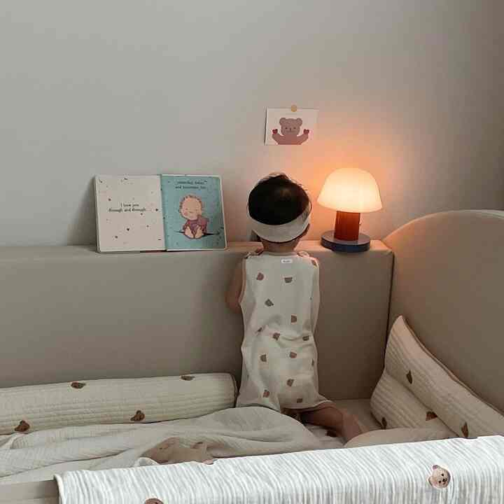 ベージュとホワイトの色調の子供部屋、ベビーバンパーベッドとテーブルランプが配置された温かみのある印象的な空間