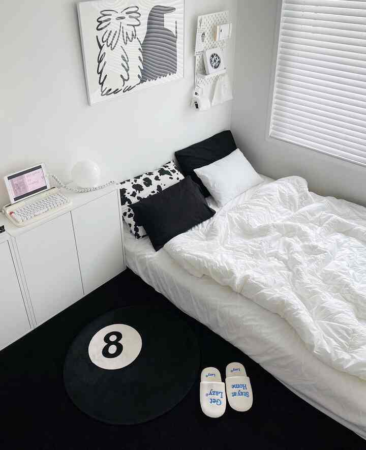 A simple monochrome black and white single household bedroom featuring corner storage cabinet and an 8-ball rug with clean aesthetics