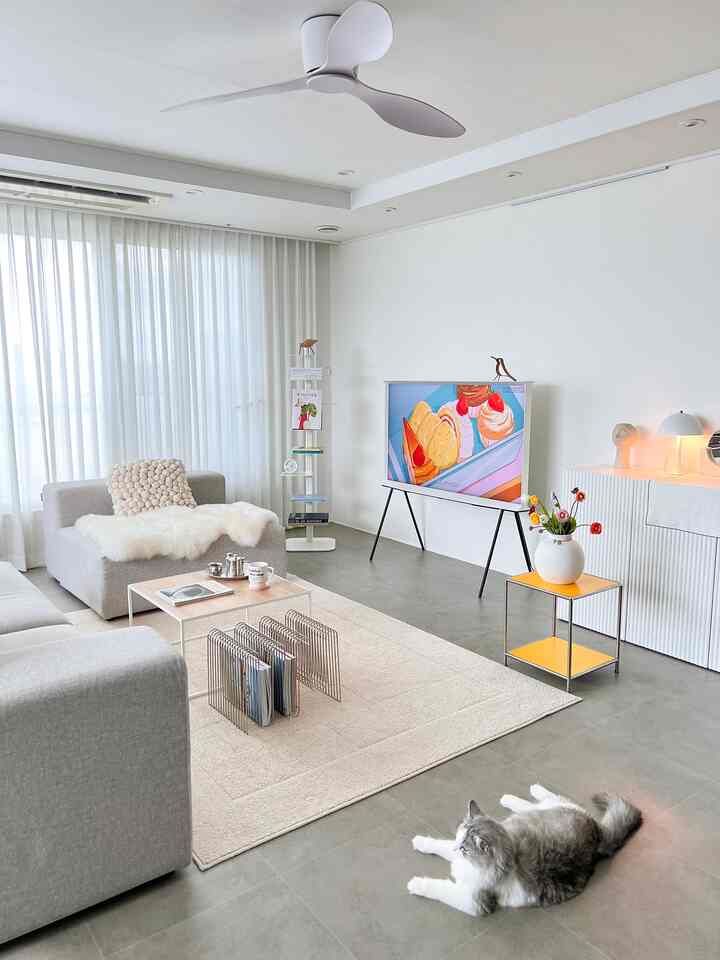 A modern living room in white tones featuring grey sofas, a rug, and a cat lying comfortably on the tiled floor, creating a clean atmosphere