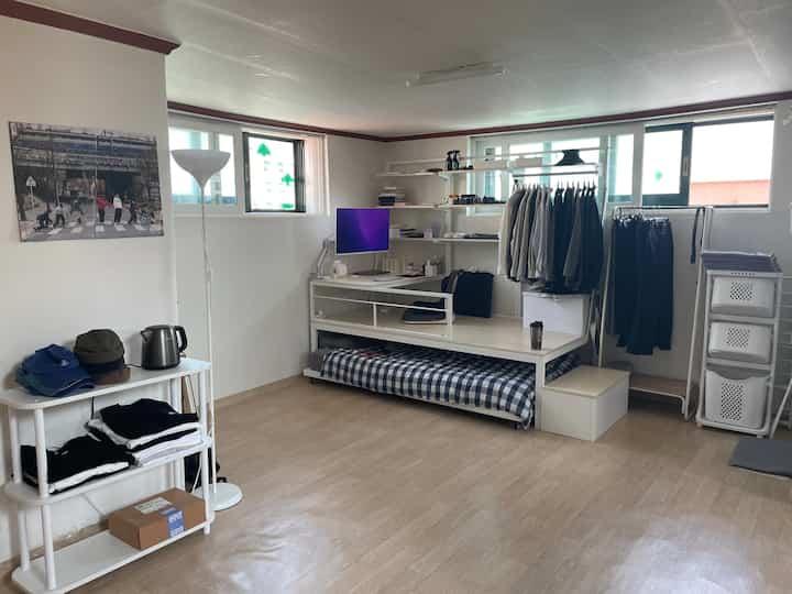 白とライトブラウンのトーンが特徴的なモダンな寝室、デスクと洋服ラックが配置された実用的な空間