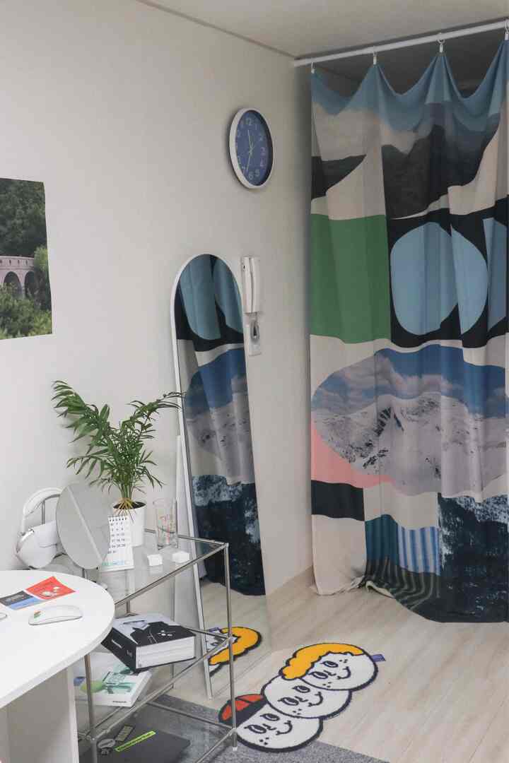 White-walled studio apartment with blue curtain room divider, featuring a colorful rug and potted plant for a cozy natural vibe