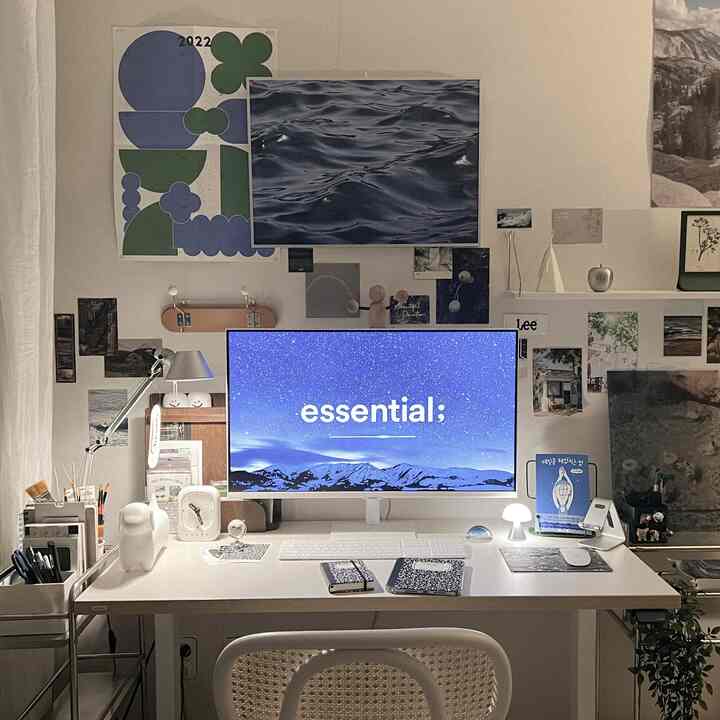 White and blue toned home office space featuring dual monitors, desk with lighting and picture frames in a clean work setup