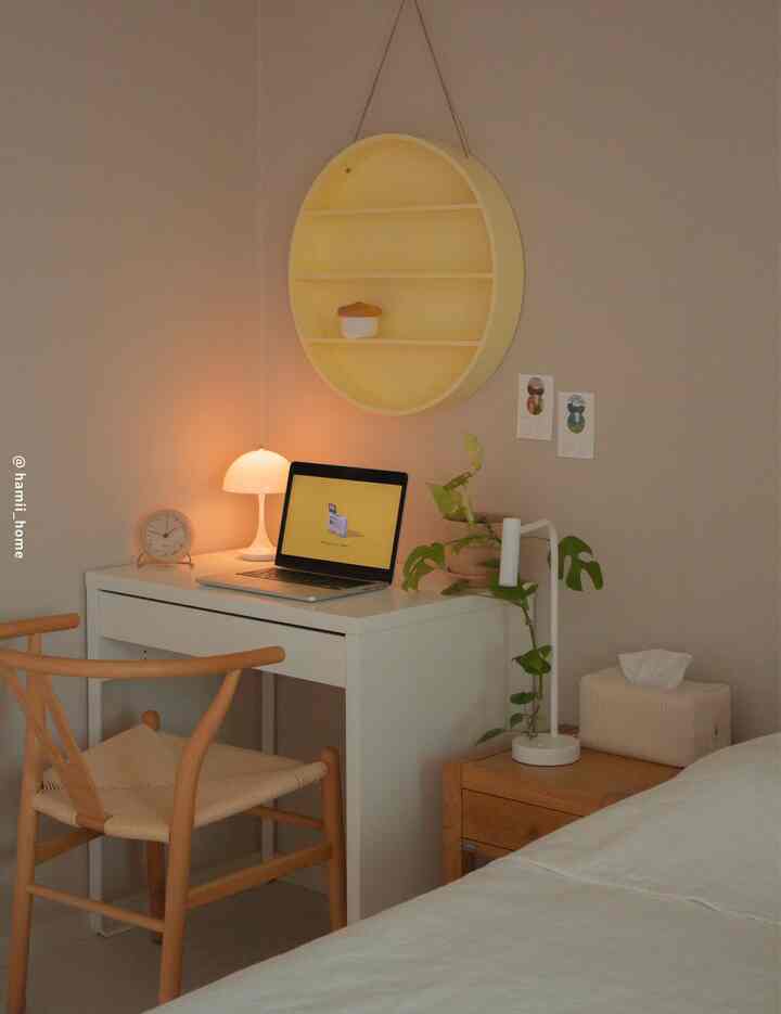 Beige-walled bedroom combined with a home office featuring wood tone furniture, a yellow circular shelf, white desk and warm lighting