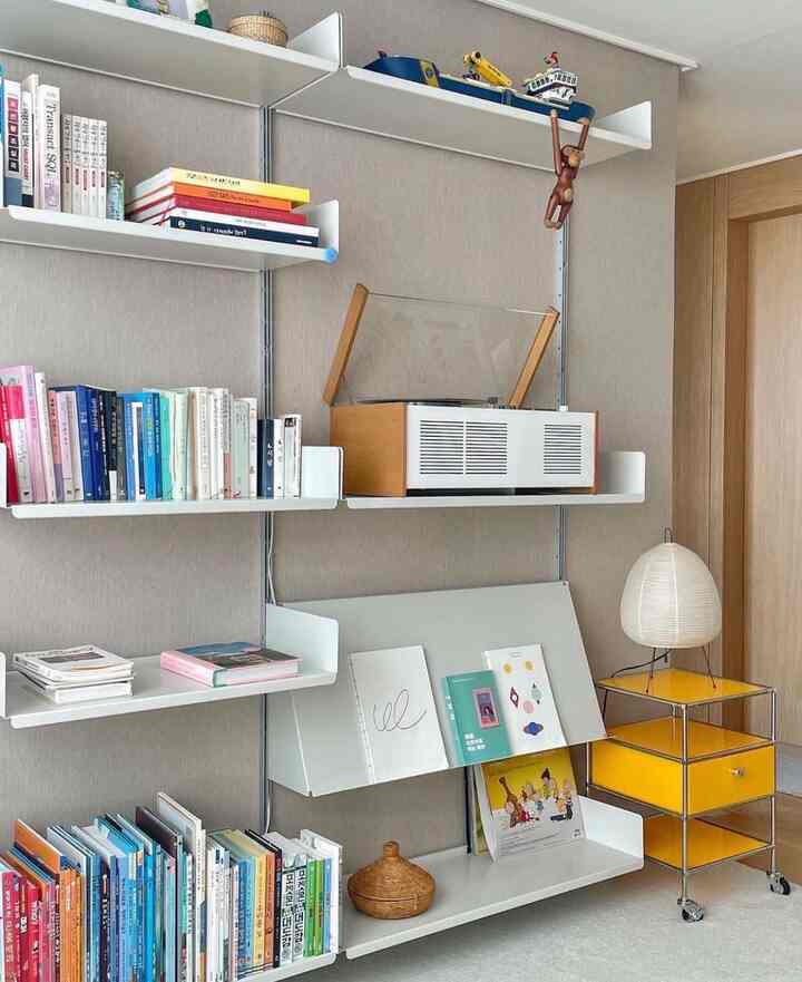 Natural modern living room corner with white and wood tone modular shelving, storage cabinet, books, objets, and lighting