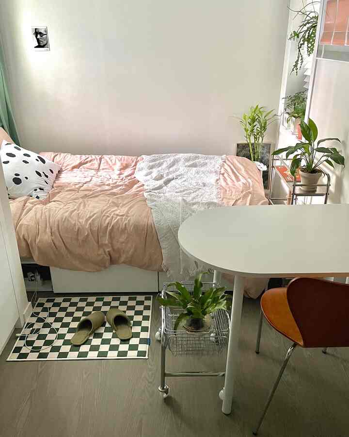 Compact bedroom with white walls and brown flooring featuring a bed and dining table creating a cozy atmosphere