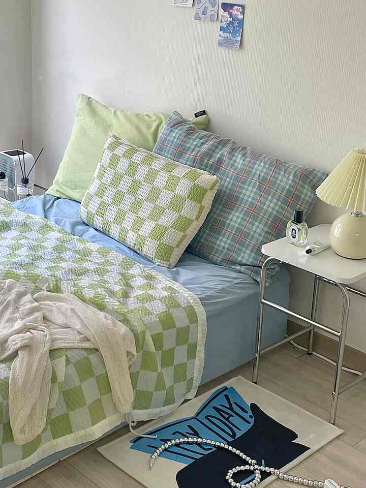 Pastel blue and green toned bedroom featuring checkered bedding, a stool, and a table lamp in a cozy setting