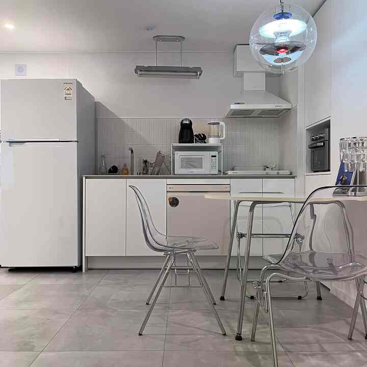 ホワイトと透明素材が調和したコンパクトなキッチン、ミッドセンチュリーモダンスタイルのダイニングテーブルと椅子が配置された清潔感のあるインテリア