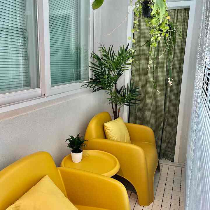 Bright yellow outdoor table and chairs arranged in a compact balcony space, featuring green plants and checkered curtains creating a natural atmosphere