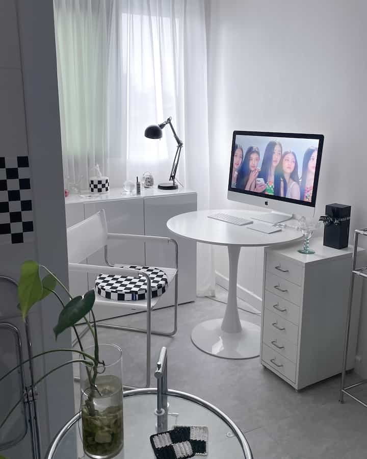 Bright white-toned home office featuring a round table, desk with computer, and checkerboard patterned chair in a clean interior