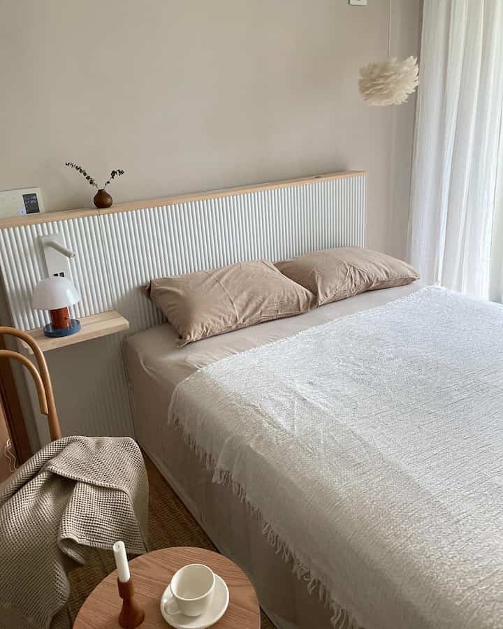 A white and wood tone bedroom featuring a tidy bed with pillows and blanket, creating a natural and serene atmosphere