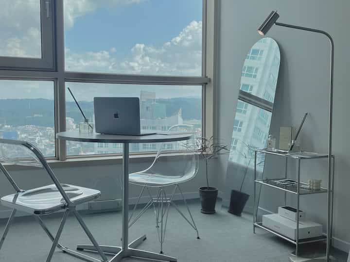 ホワイトとグレーのモノトーンのホームオフィス、透明な椅子と丸テーブル、ミニマルな家具が配置された雰囲気のあるインテリア