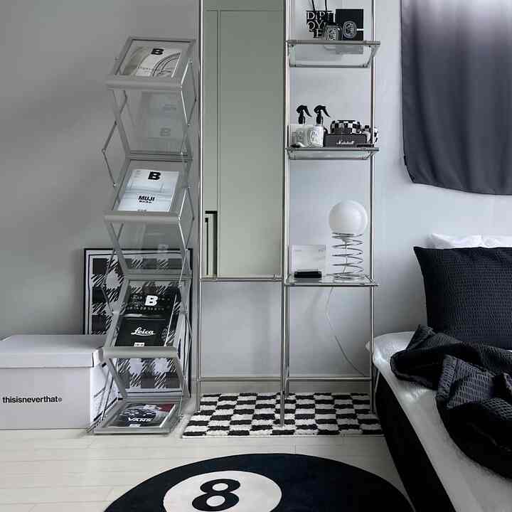 モノトーンの寝室空間、黒い寝具とチェッカーボードのラグ、金属の棚とポスターが調和した印象的なインテリア