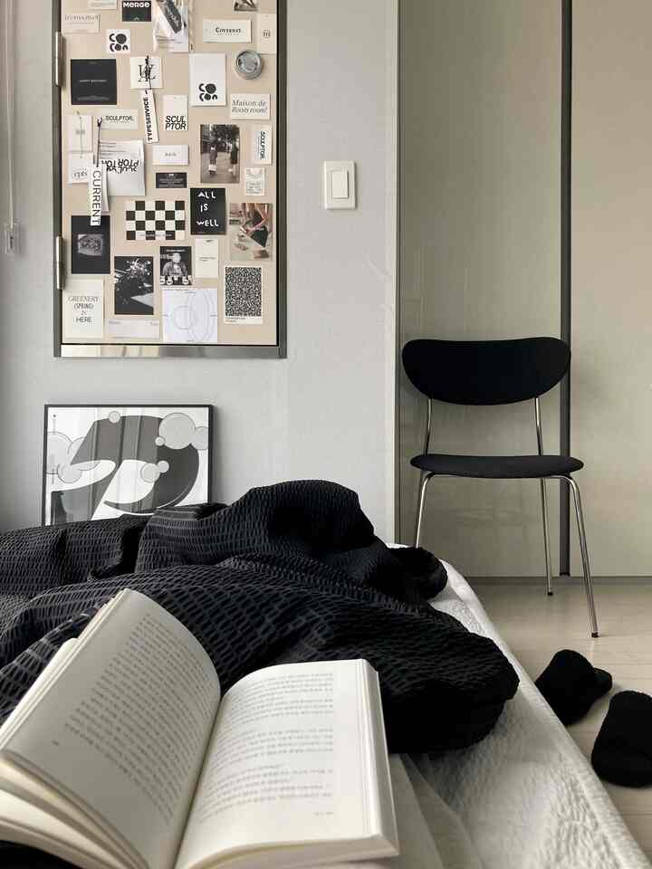黒と白のトーンの寝室、黒い寝具と椅子、壁にウォールデコとポスターが配置されたシンプルな空間