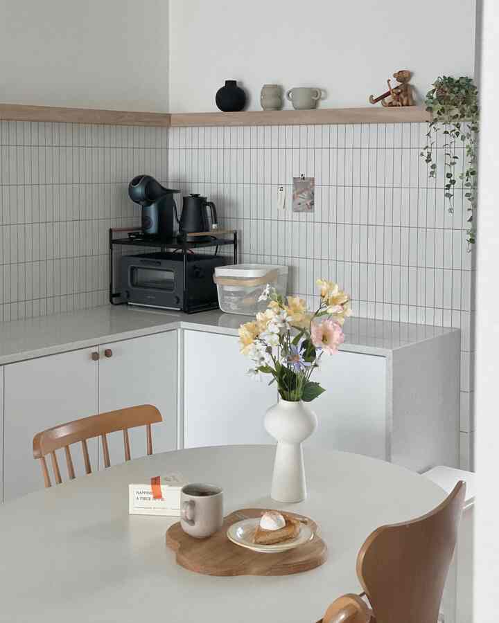 ホワイトと木目調が調和したシンプルで清潔感のあるキッチン、おうちカフェの雰囲気を感じさせるテーブルと装飾品配置
