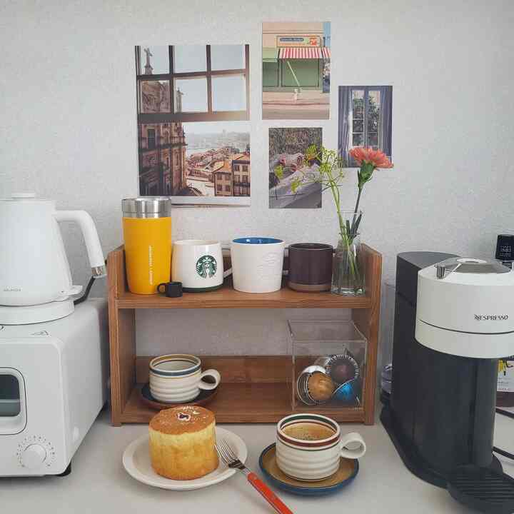 Cozy home cafe space featuring white background walls, wood tone shelves with mugs, electric kettle, and coffee machine