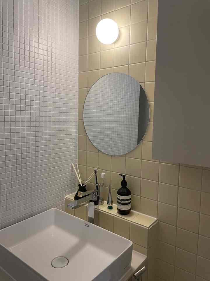 ベージュとホワイトのタイルが調和するバスルーム、丸い鏡とシンプルな洗面台が清潔感のある雰囲気のインテリア