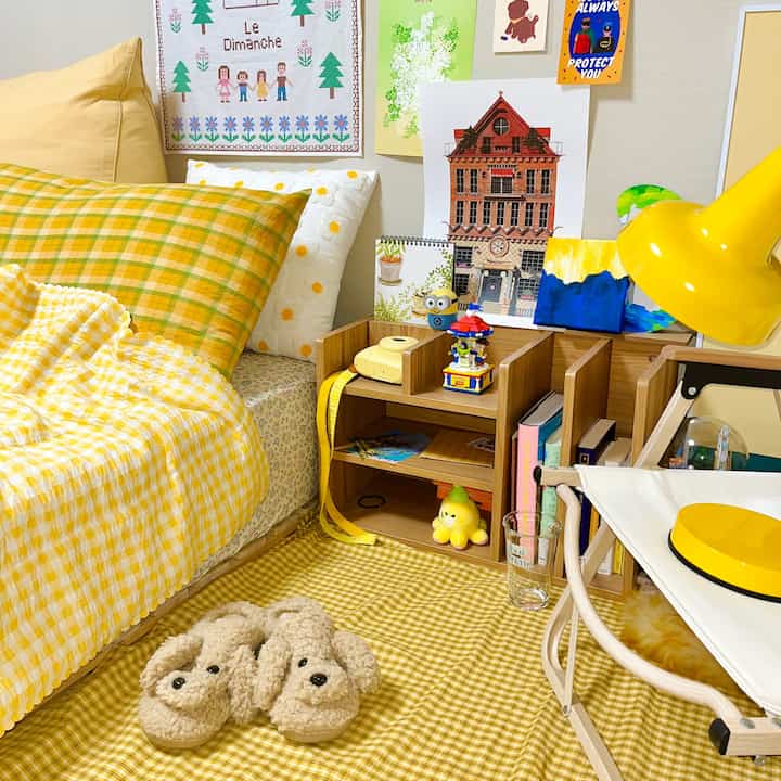 Yellow and wood tone bedroom featuring a checked duvet cover, various cushions, and charming small decor for a cozy atmosphere
