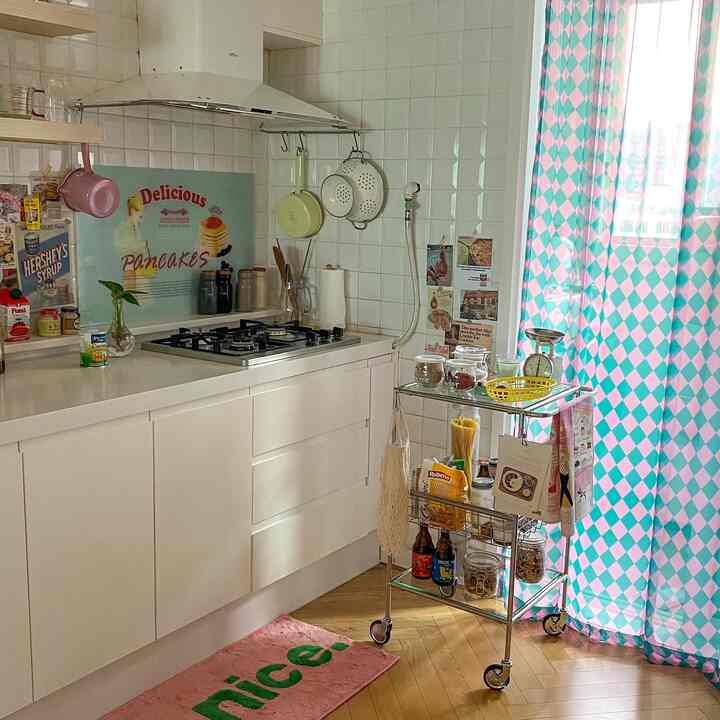Modern kitchen space with white tiled walls, stainless steel storage cart and pink-mint patterned curtains