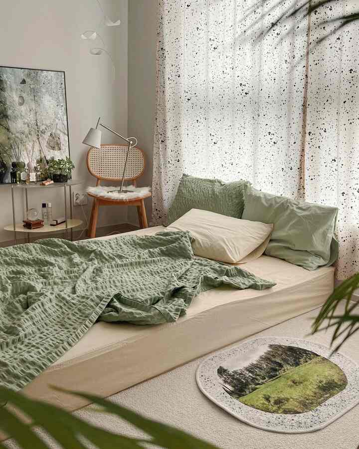 A soft green and natural wood-tone bedroom featuring a rattan chair and speckled curtains creating a calm natural ambiance