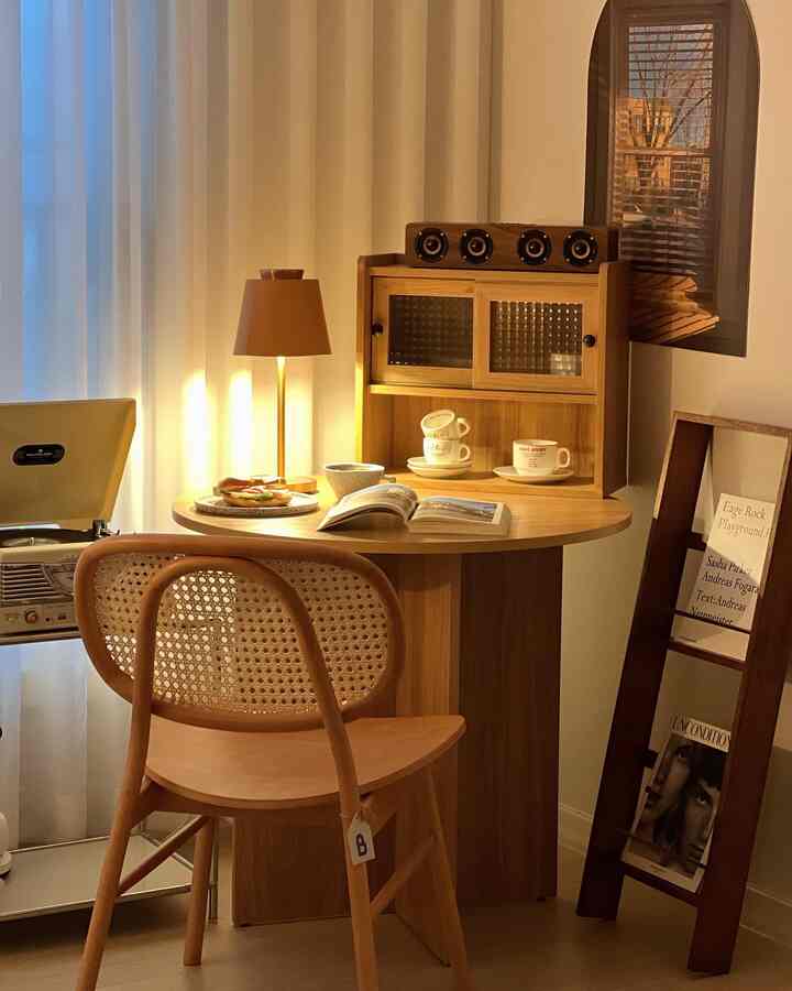 Warm wood tones and beige hues define a cozy home cafe space with a round dining table, rattan chair, and table lamp