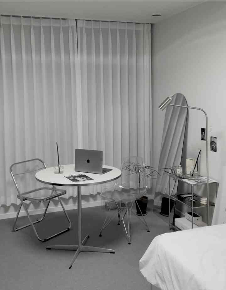 Simple bedroom and home office space in white and transparent tones featuring a round table and clear chairs, creating a cozy atmosphere