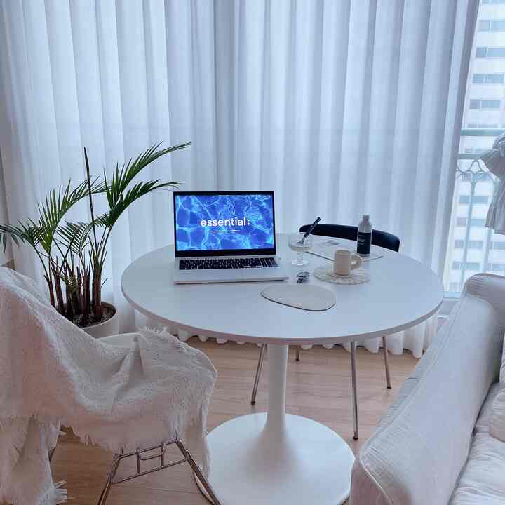 White-toned living room featuring a round table, sofa, and greenery, creating a modern and calm interior atmosphere