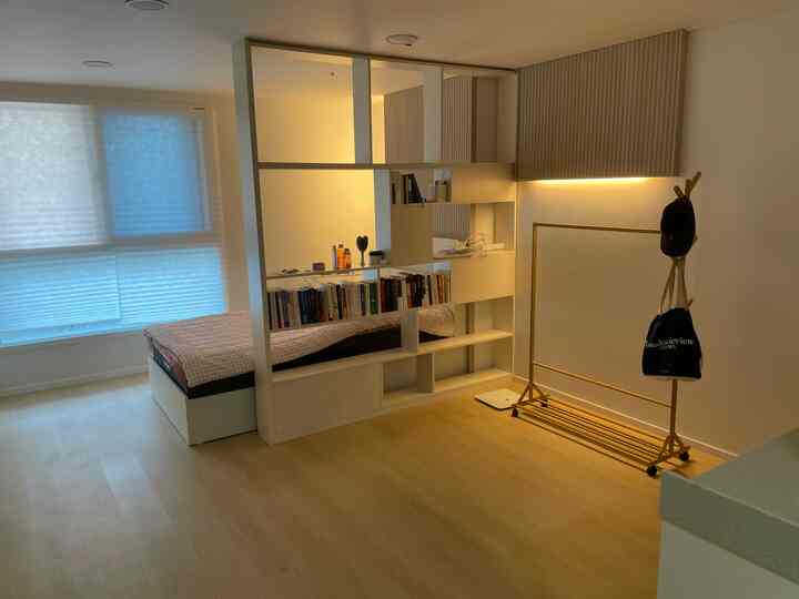 Bright white and natural toned bedroom featuring a partition bookshelf and bed with a clean, minimal atmosphere