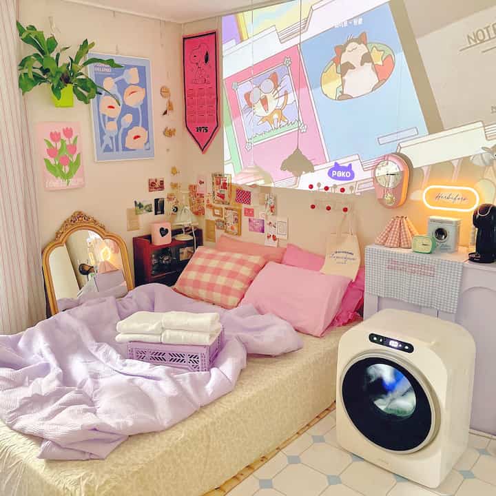 Cozy bedroom with pink and purple tones featuring decorative posters and a wall clock, accented by indoor plants.