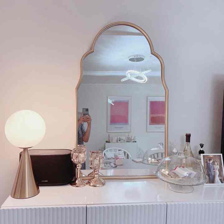 White and gold-toned living room featuring large gold-framed mirror and various interior accessories in a stylish setting