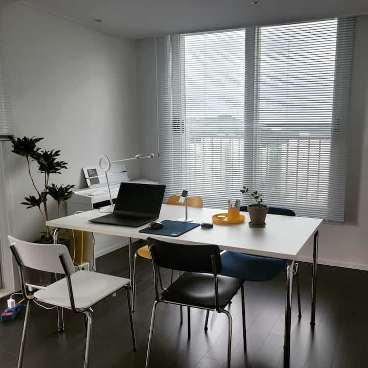 White and black toned home office space featuring a central table with multiple chairs, a laptop, and lighting for a neat workspace