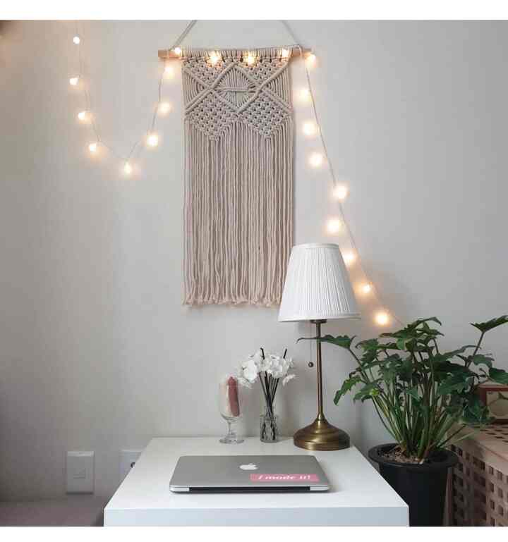 白と木目調の組み合わせの書斎風ワンルーム作業スペース、マクラメの壁掛けとムードランプ、植物が落ち着いた雰囲気を演出