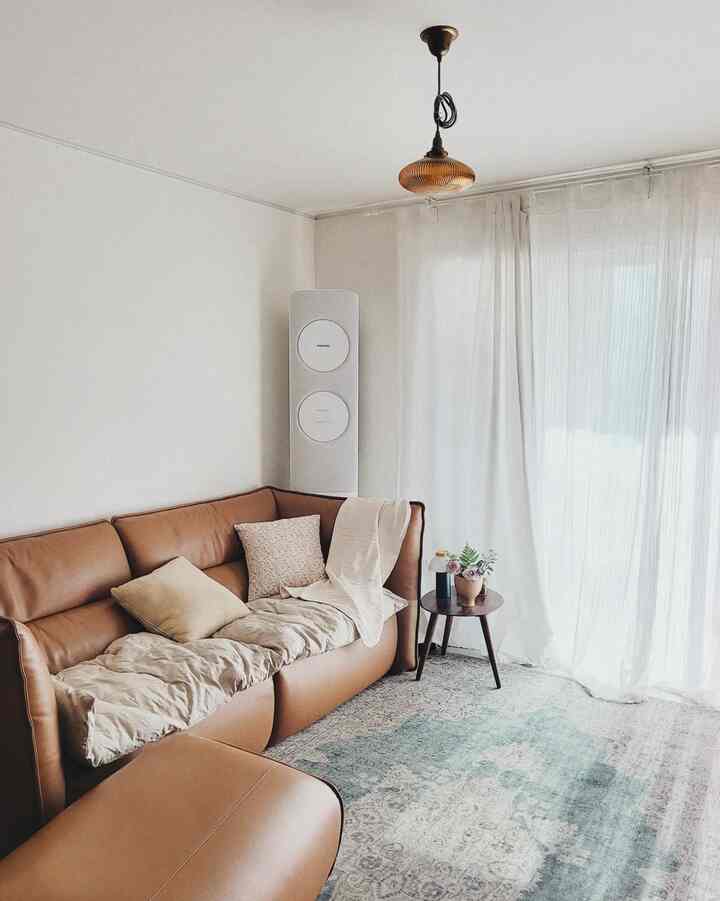 Living room with white walls and curtains featuring a brown leather sofa conveying a warm atmosphere