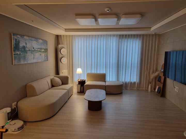 ベージュと白のトーンのリビング、シンプルなソファとコーヒーテーブル、大きな窓とカーテンが調和した落ち着いた空間