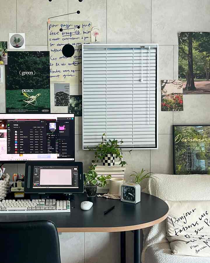 A home office space with gray blinds and various posters on the wall, featuring a black desk setup