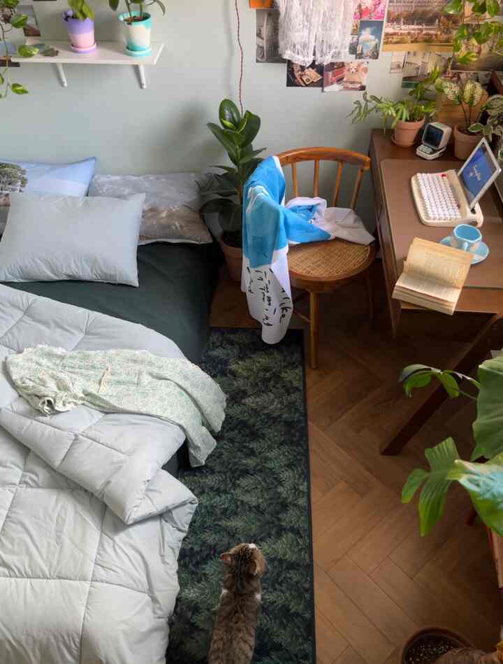 やわらかなグリーントーンの寝室、木製家具、植物のあるデスク、猫がいる雰囲気のあるインテリア