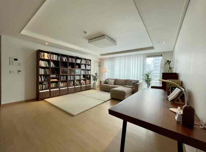 Natural wood-toned living room featuring large bookshelf and beige sofa in a study-like setting