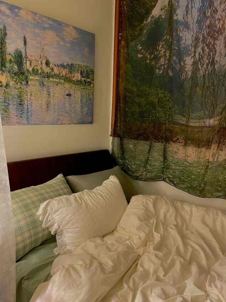 緑のトーンが主な寝室、モネのポスターと自然の風景が描かれたカーテンが配置された雰囲気のあるヴィンテージスタイルの空間