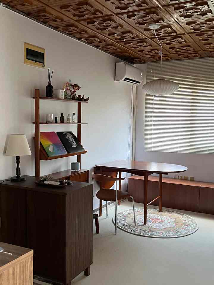 木目調が際立つリビング、ベージュのブラインド、木製家具とペンダントライトが配置されたシンプルで自然な雰囲気の空間