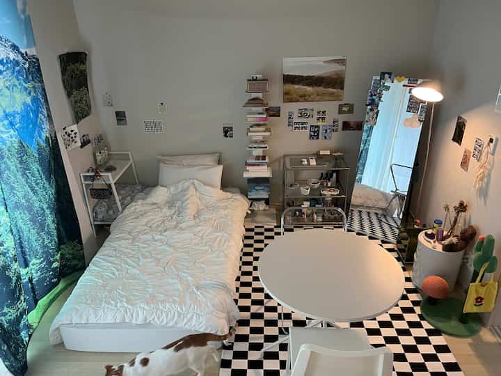 白と黒のモノトーンで6畳の寝室兼リビング、中央にベッドと丸いテーブル、右側に大きな鏡とフロアランプが配置されたインテリア