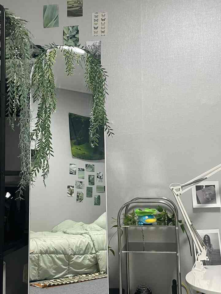 淡いグリーンとナチュラルカラーの寝室、全身鏡とサイドテーブル、緑の植物が配置された雰囲気のあるインテリア