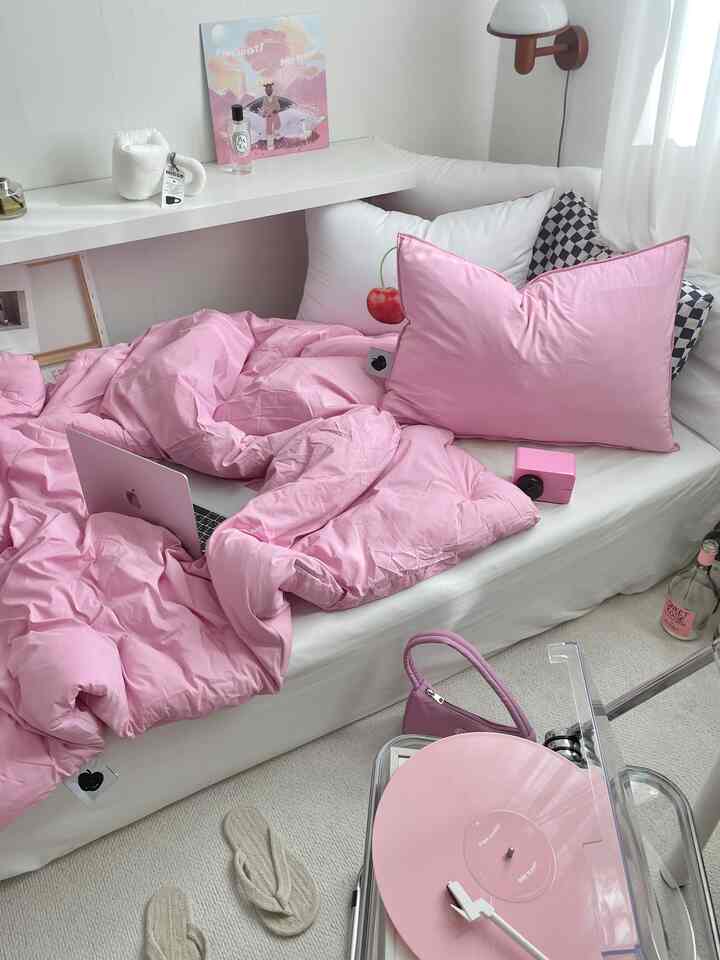 Small bedroom in white and pink tones featuring a cozy bed with pink bedding, pillows, and a vintage-style turntable