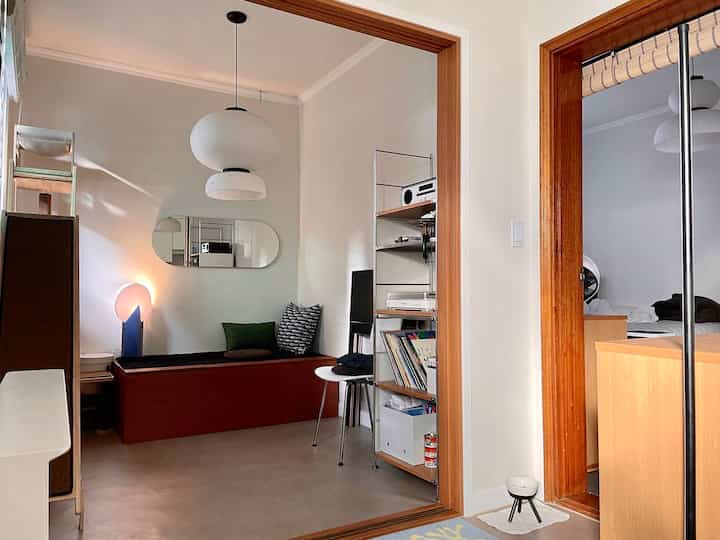 Minimal living room with white and wood tones featuring a bench sofa, pendant lights, and a bookshelf creating a cozy atmosphere