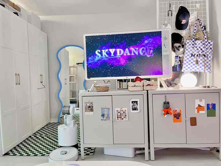 Narrow living room with white walls and green checkerboard floor, featuring multiple cabinets, a TV stand, cat photos, and a cat tower in a mid-century modern style