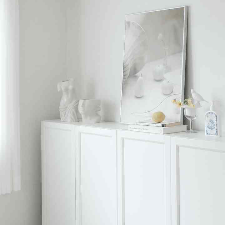 明るいホワイトトーンの壁とキャビネットの上にオブジェとポスターが配置されたミニマルで自然な雰囲気のある空間