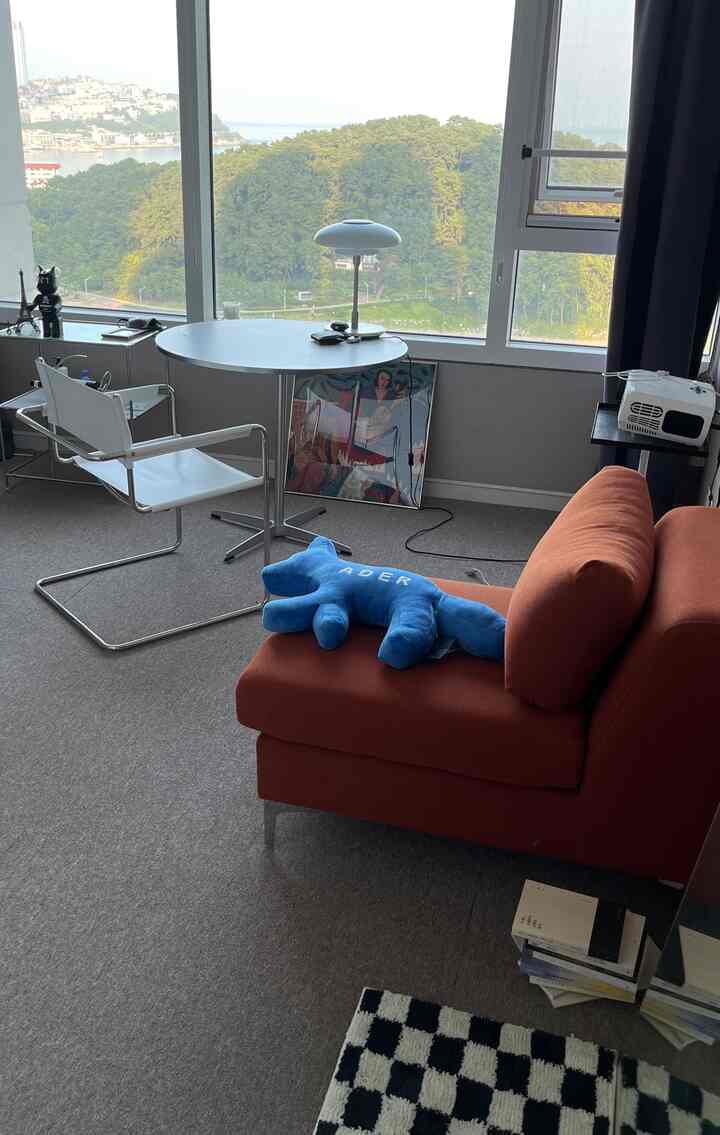 オレンジ色のソファと丸テーブル、白いアームチェアが配置されたコンパクトな部屋、海雲台の海が見えるインテリア